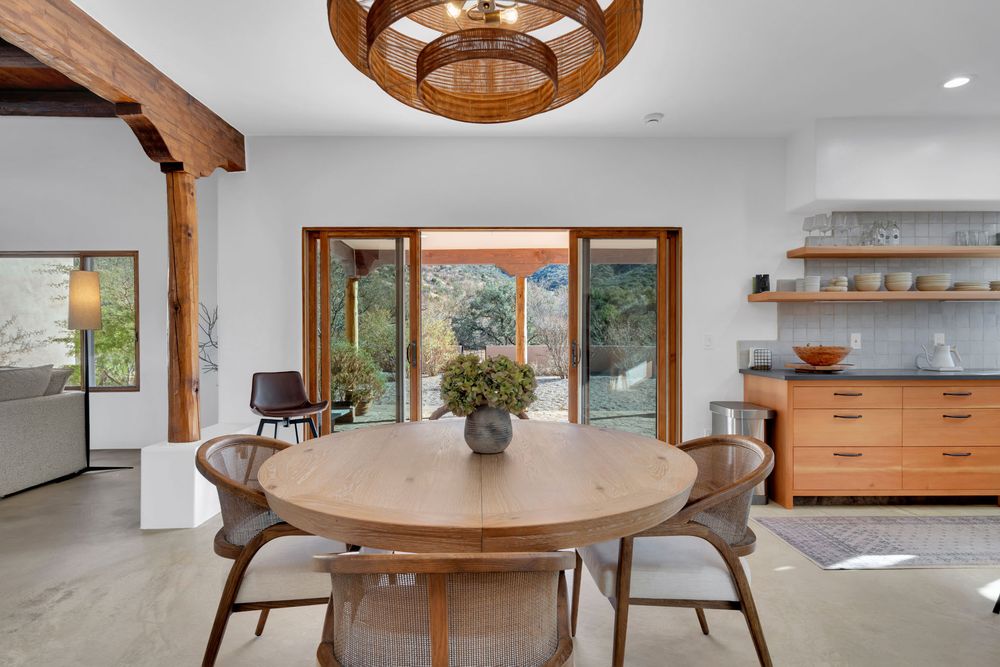 Modern dining room with round wooden table, gray chairs, wood beam accent and circular pendant light above.