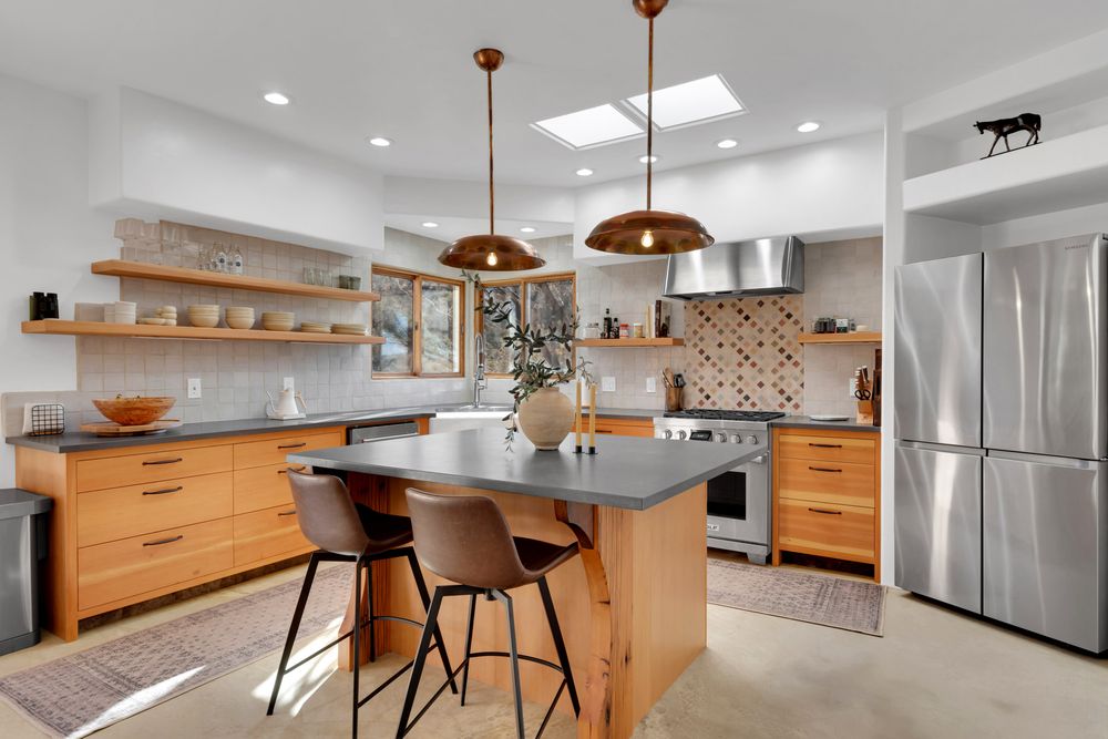 Modern kitchen with wooden cabinets, copper pendant lights, and stainless steel appliances features open shelving and island seating.