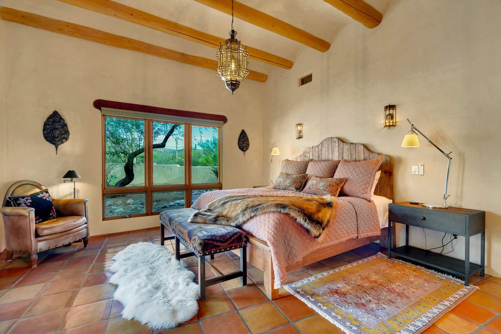 Luxurious bedroom suite with exposed wooden beams, large windows, and modern furnishings in a desert-style home.