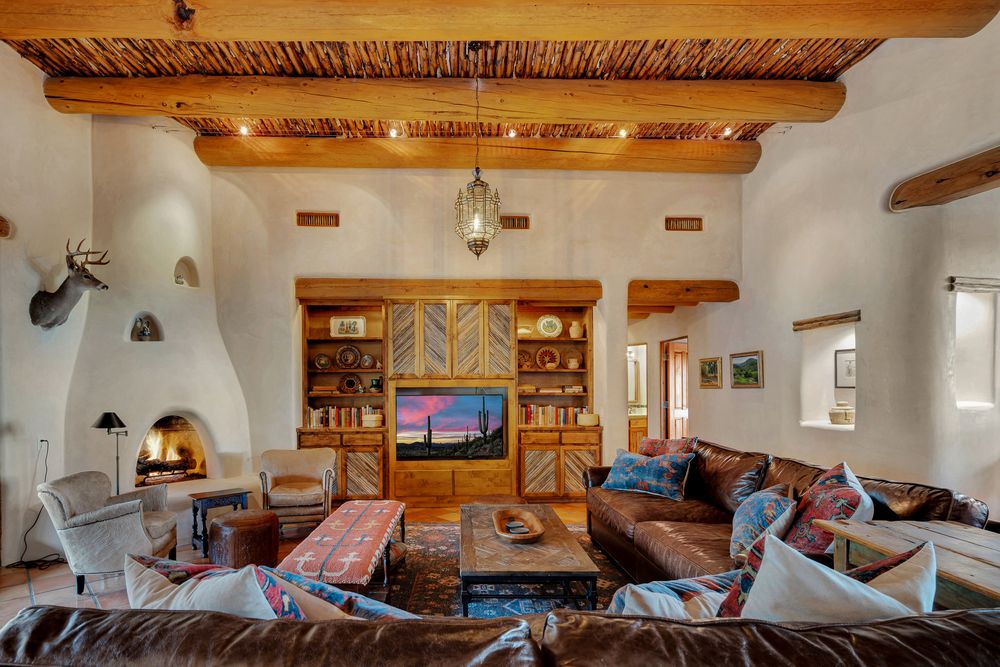Rustic living room with exposed wooden beams, white walls, and comfortable seating arranged around a TV area.