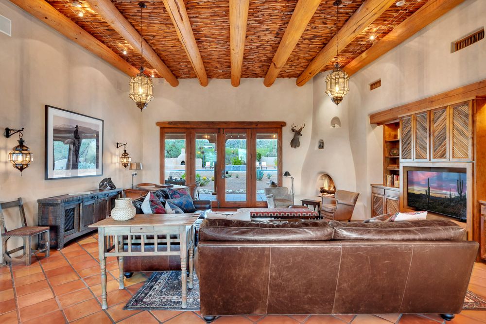Southwestern living room with exposed wood beams, terracotta floors, leather sofas and French doors leading to outdoor patio.