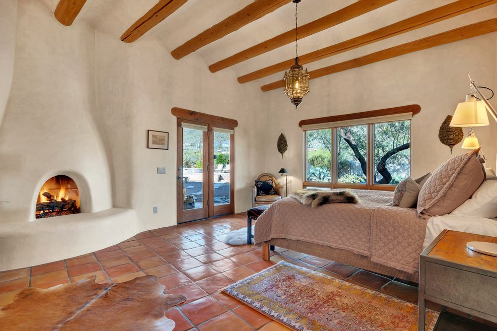 Cozy southwestern living room with kiva fireplace, exposed wooden beams, terracotta floors and corner windows.
