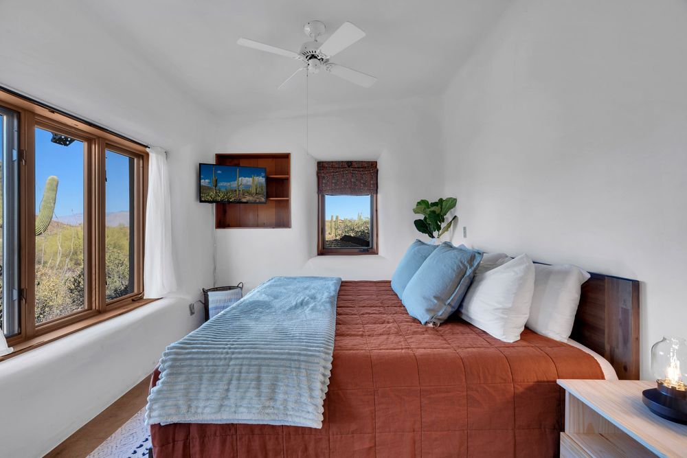 A modern bedroom interior with wood-framed windows, white walls, and blue bedding in a sunny space.