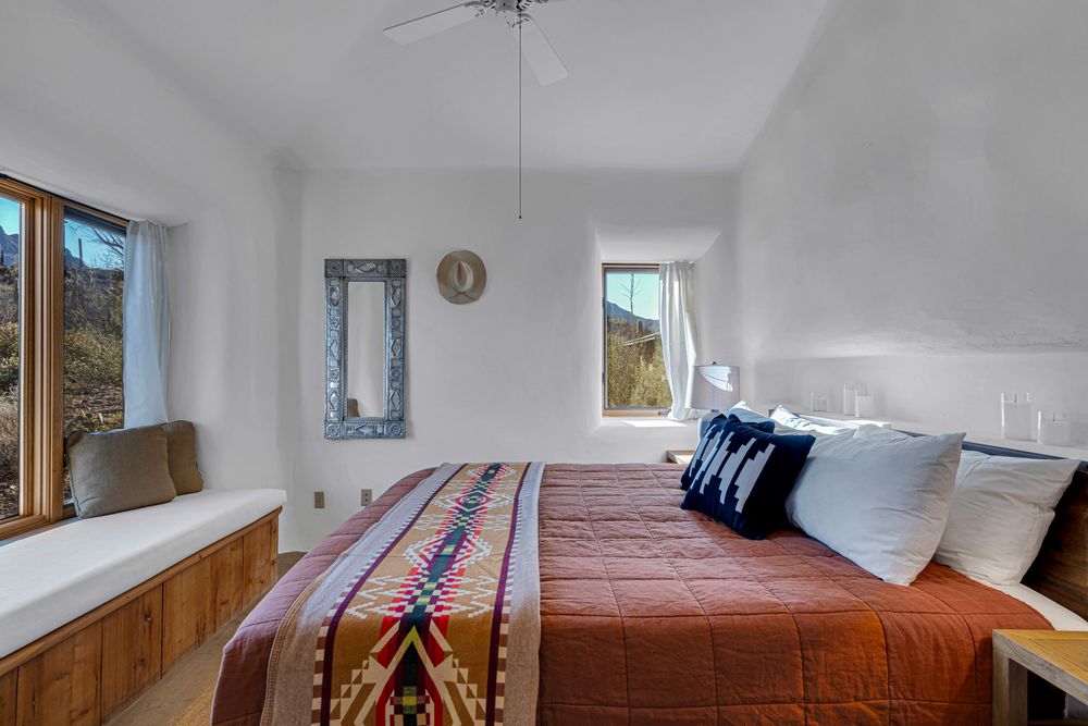 Modern bedroom interior with white walls, wooden accents, and natural light streaming through windows.