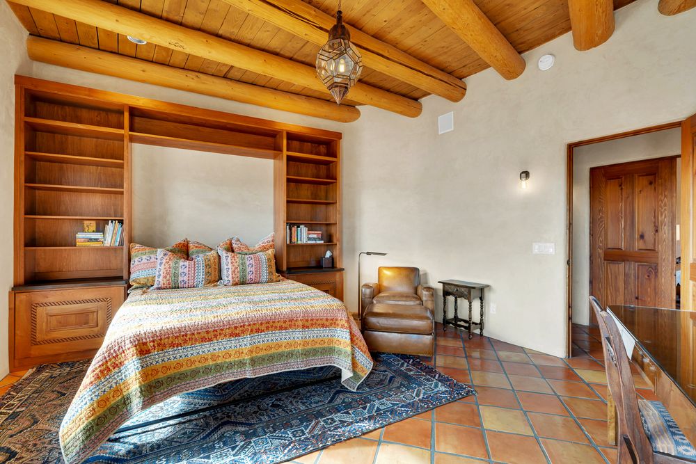 Rustic bedroom with exposed wooden beams, ceiling fan, and terracotta tile floors in a southwestern style home.