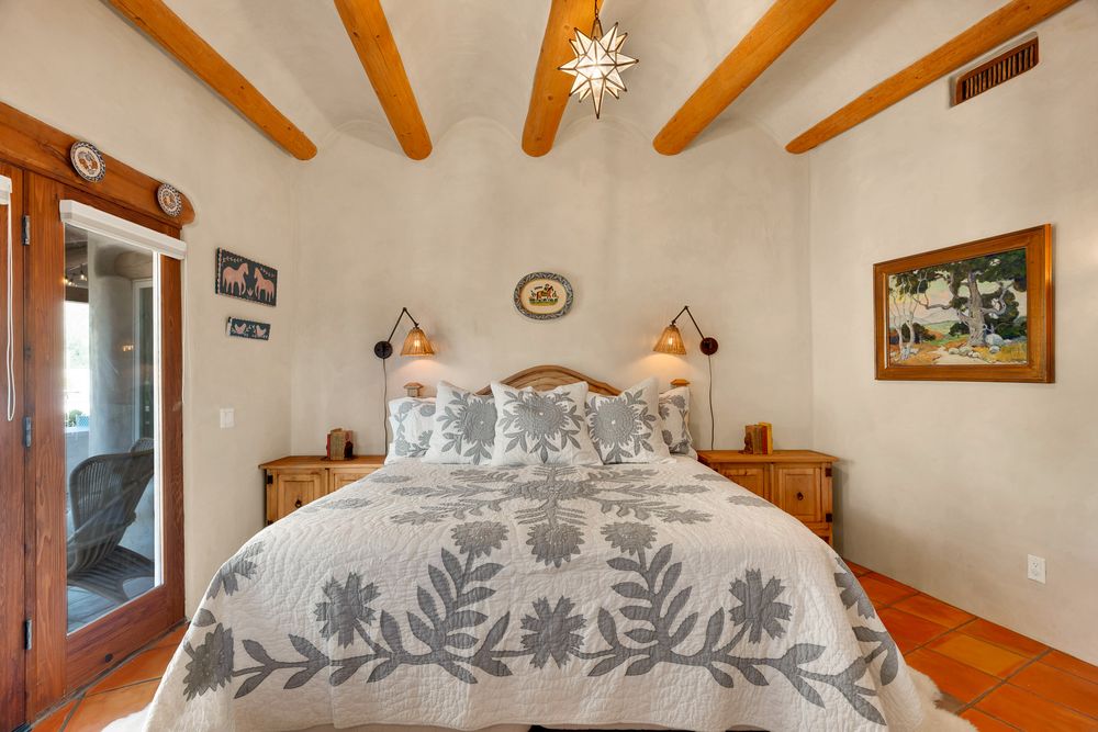 Cozy bedroom interior featuring exposed wooden ceiling beams, white walls, and decorative floral bedding.
