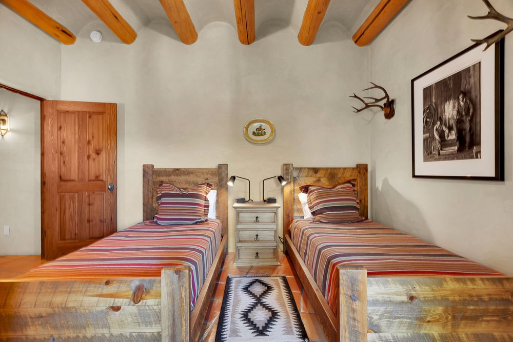 Twin rustic wooden beds with striped bedding and mounted antlers in a southwestern-style bedroom with exposed beams.