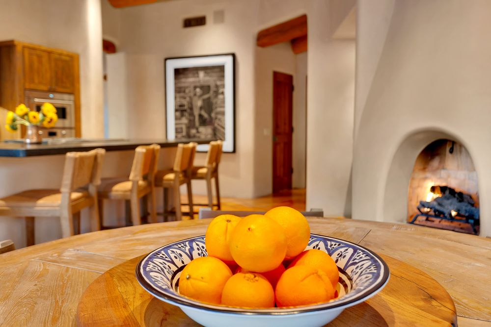 Fresh oranges in a decorative bowl on a wooden table with a cozy southwestern-style interior featuring a fireplace.