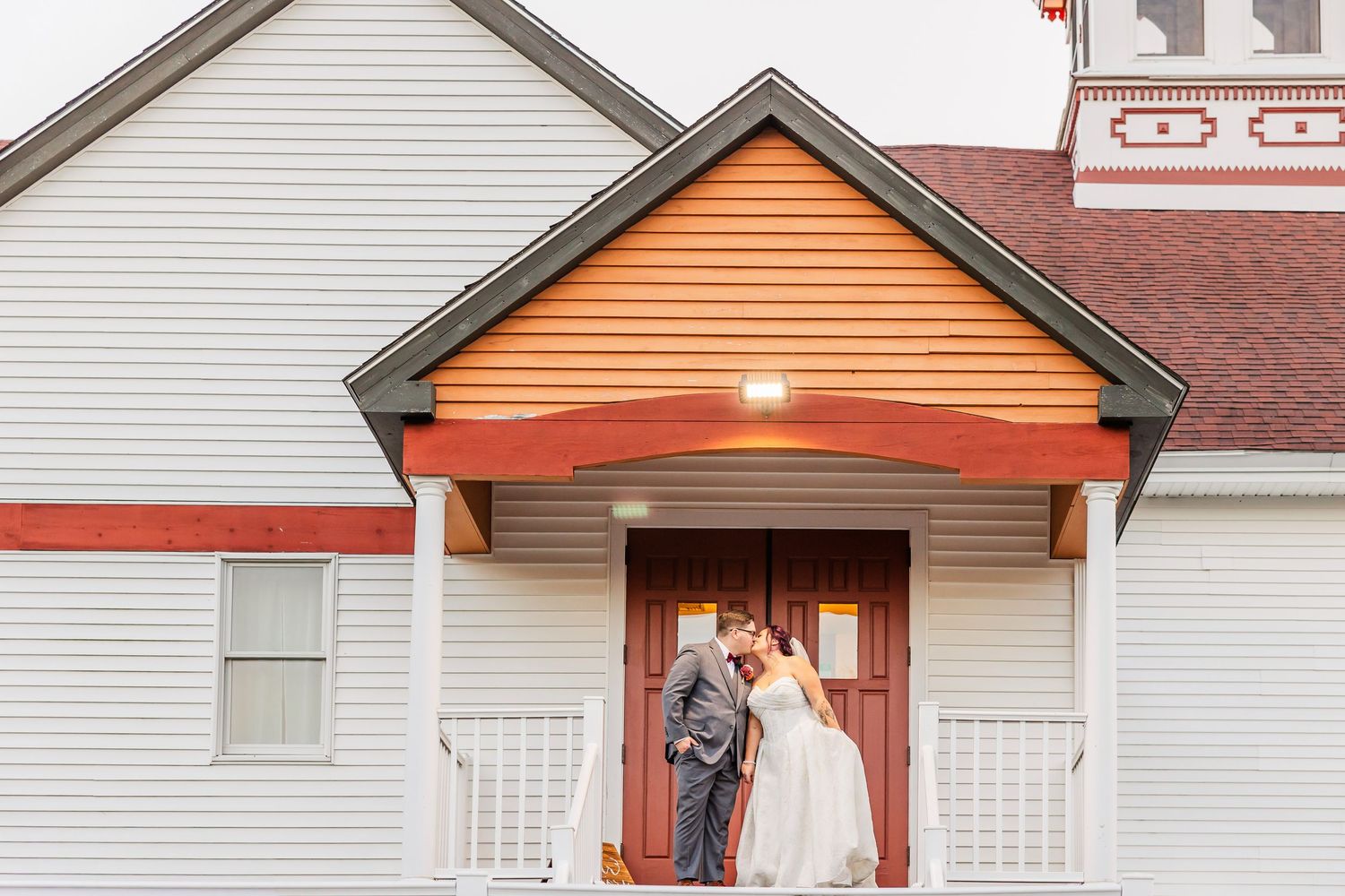 A white house with orange accents and a porch light glowing in the evening.