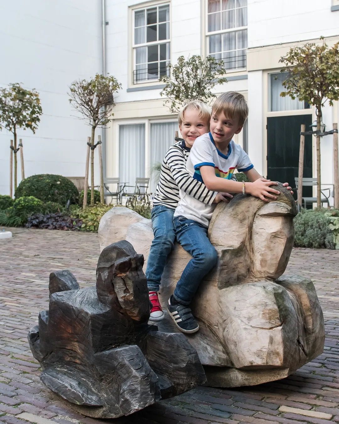 Two children sitting on a stone sculpture in a peaceful Amsterdam courtyard.