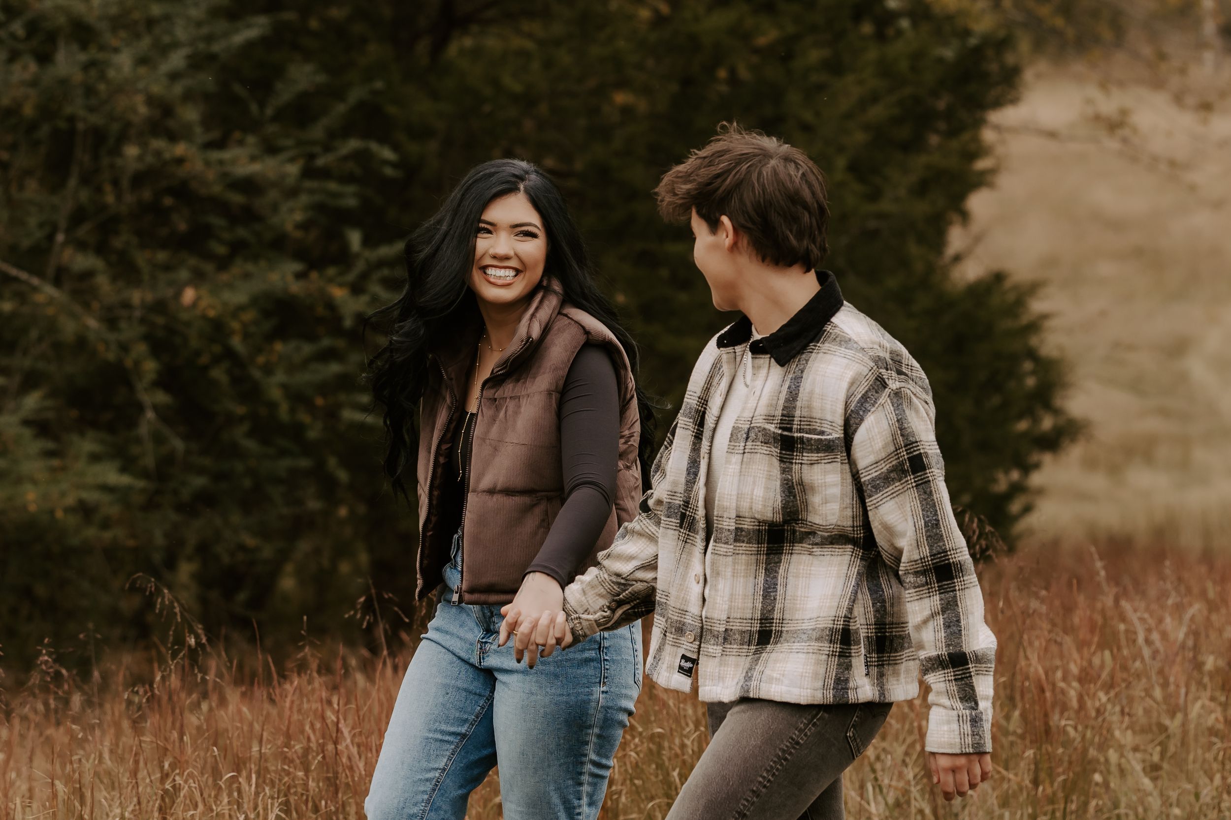 Happy couple holding hands while walking through a golden autumn field.