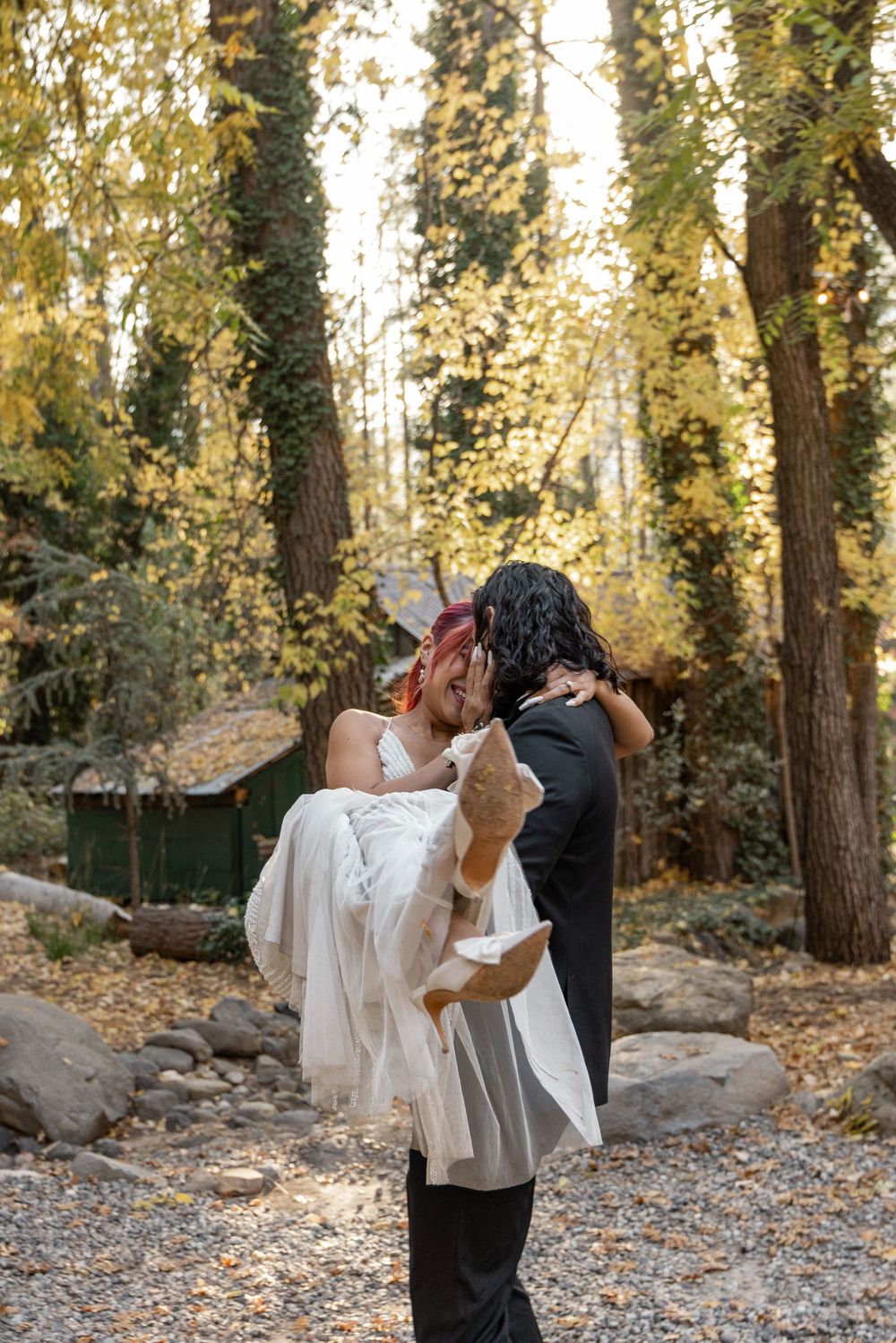 A romantic couple shares an intimate dance among tall trees in a wooded outdoor setting at sunset.