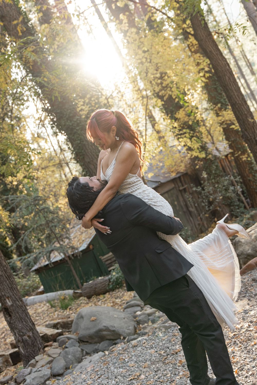 A romantic couple dances and dips in a wooded outdoor setting during golden hour sunlight.