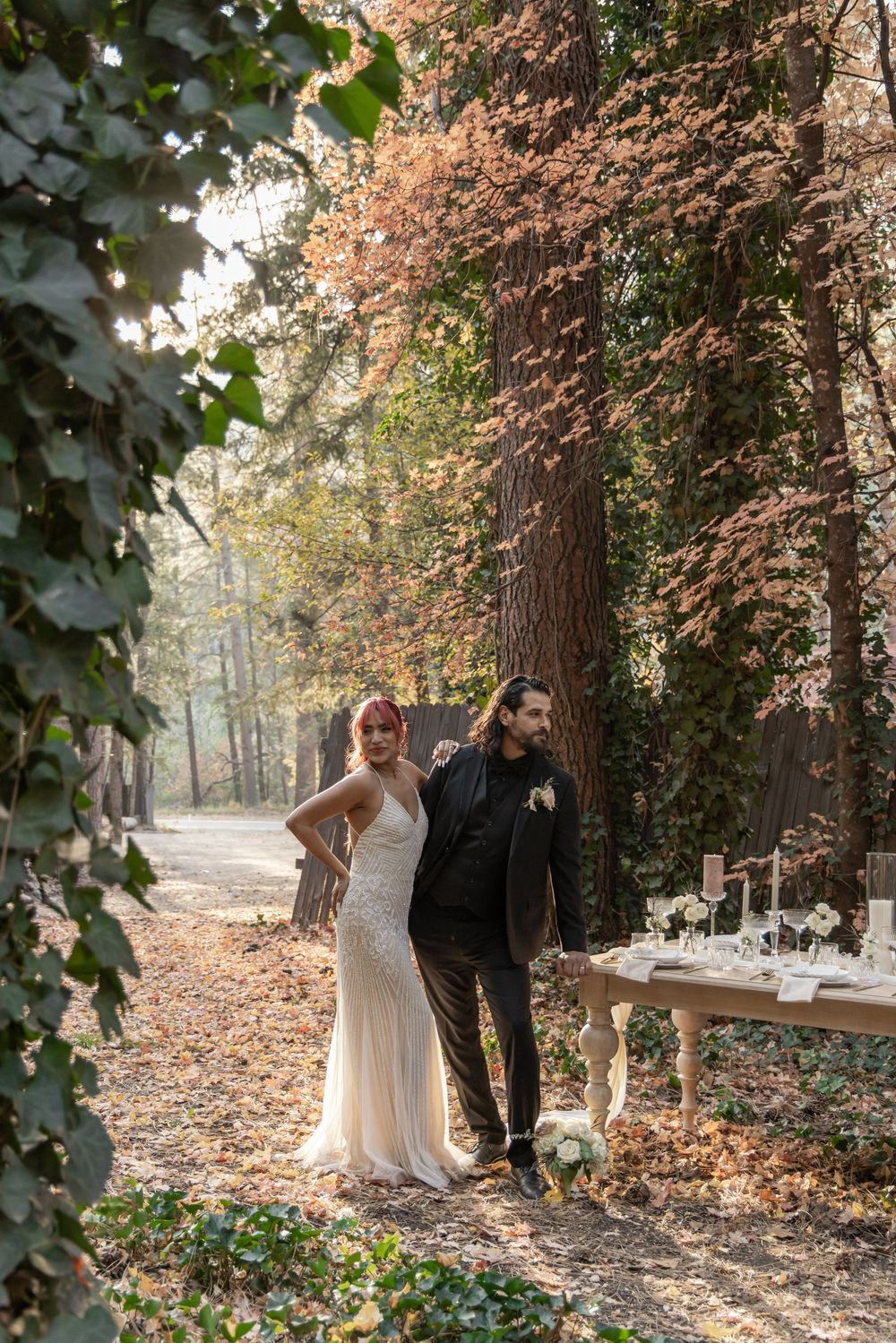 Newlyweds share an intimate moment among trees with autumn foliage in a forest setting.