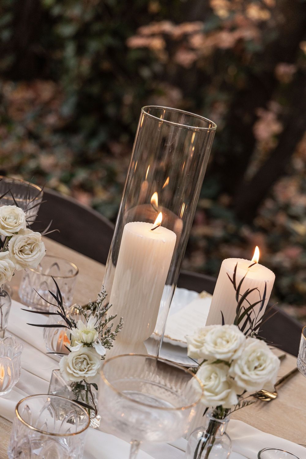 Elegant wedding table decor features white roses and glowing candles in glass cylinders.