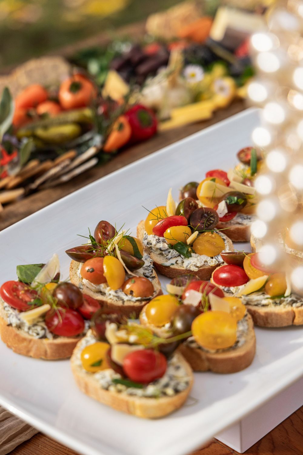 Colorful bruschetta appetizers topped with cherry tomatoes and herbs served on a white platter at a catered event.