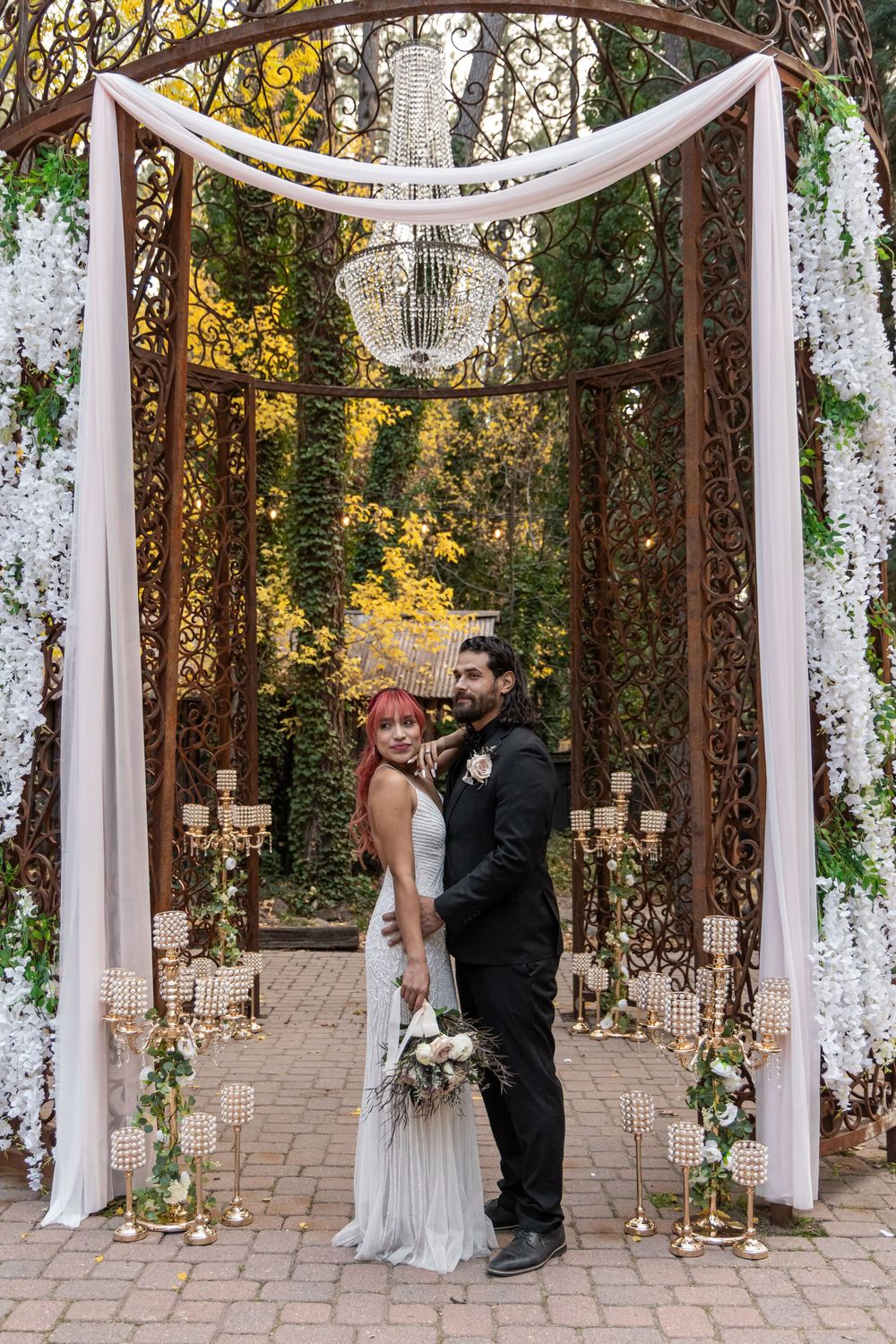 Outdoor wedding ceremony setup with white drapes and natural foliage in a garden setting.