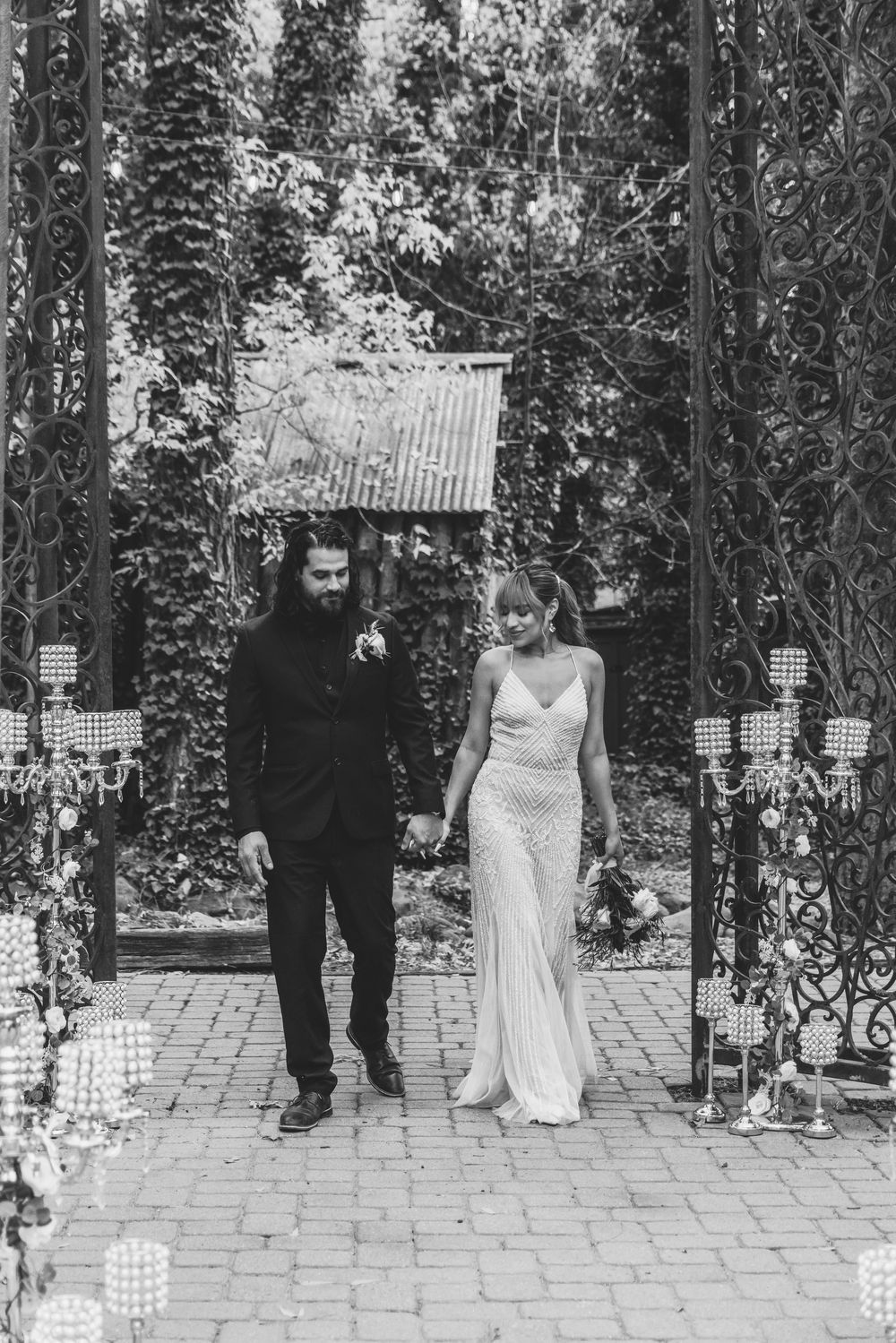 Black and white photos show a couple walking under a decorative archway with string lights.