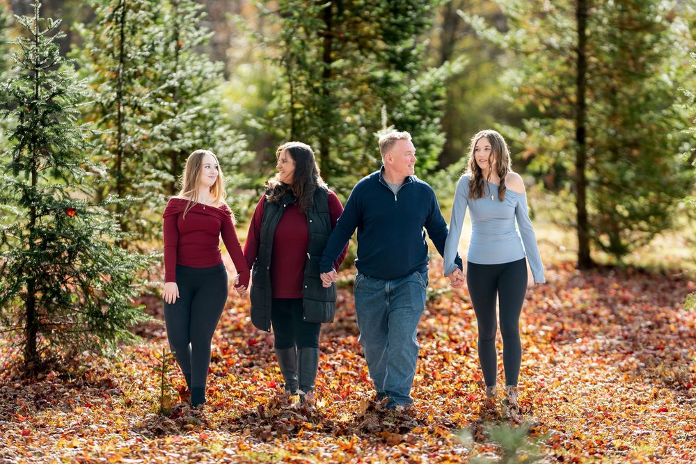 Happy family of four walking hand-in-hand through a scenic Christmas tree farm in autumn.