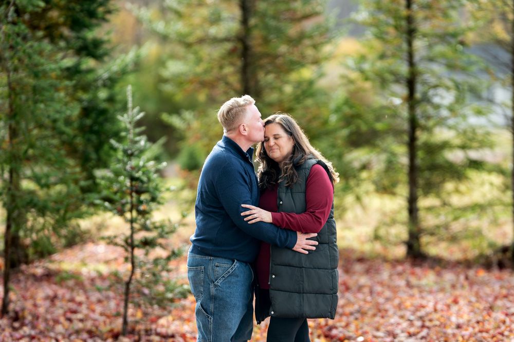 Romantic couple sharing a tender moment among evergreen trees in an autumn forest setting.