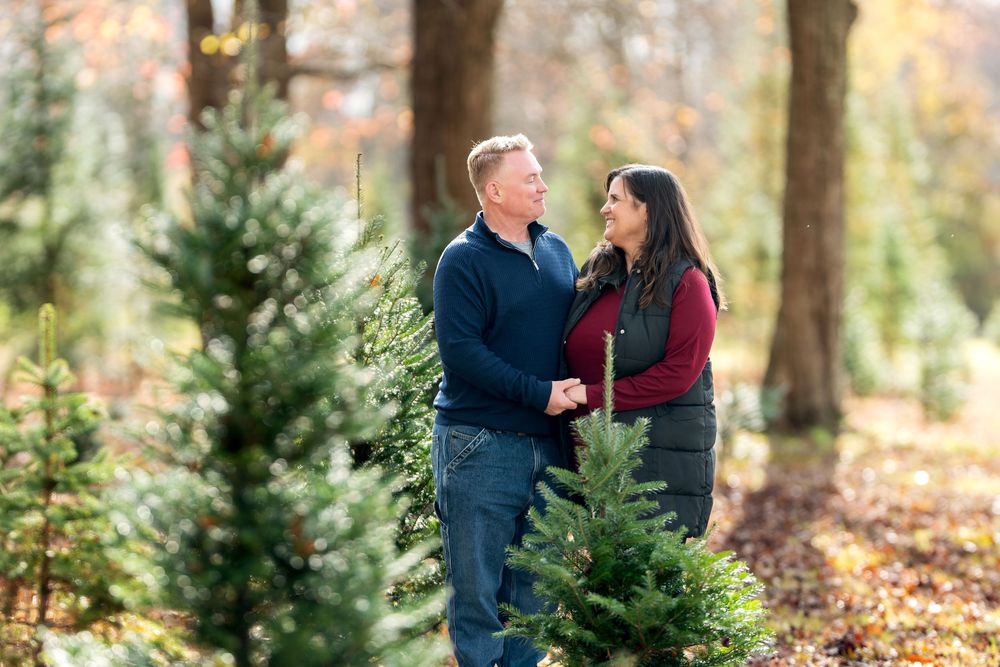 Couple holding hands and smiling at each other among evergreen trees in autumn forest.