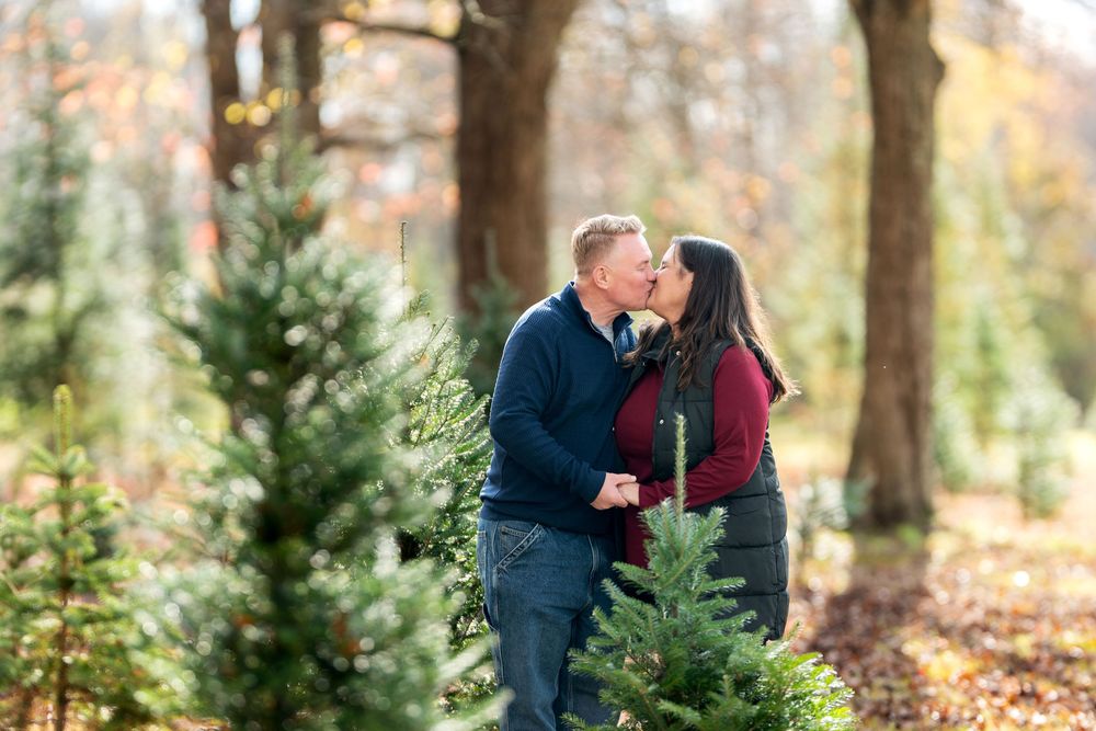 Romantic couple sharing a kiss surrounded by small pine trees in colorful fall woods.
