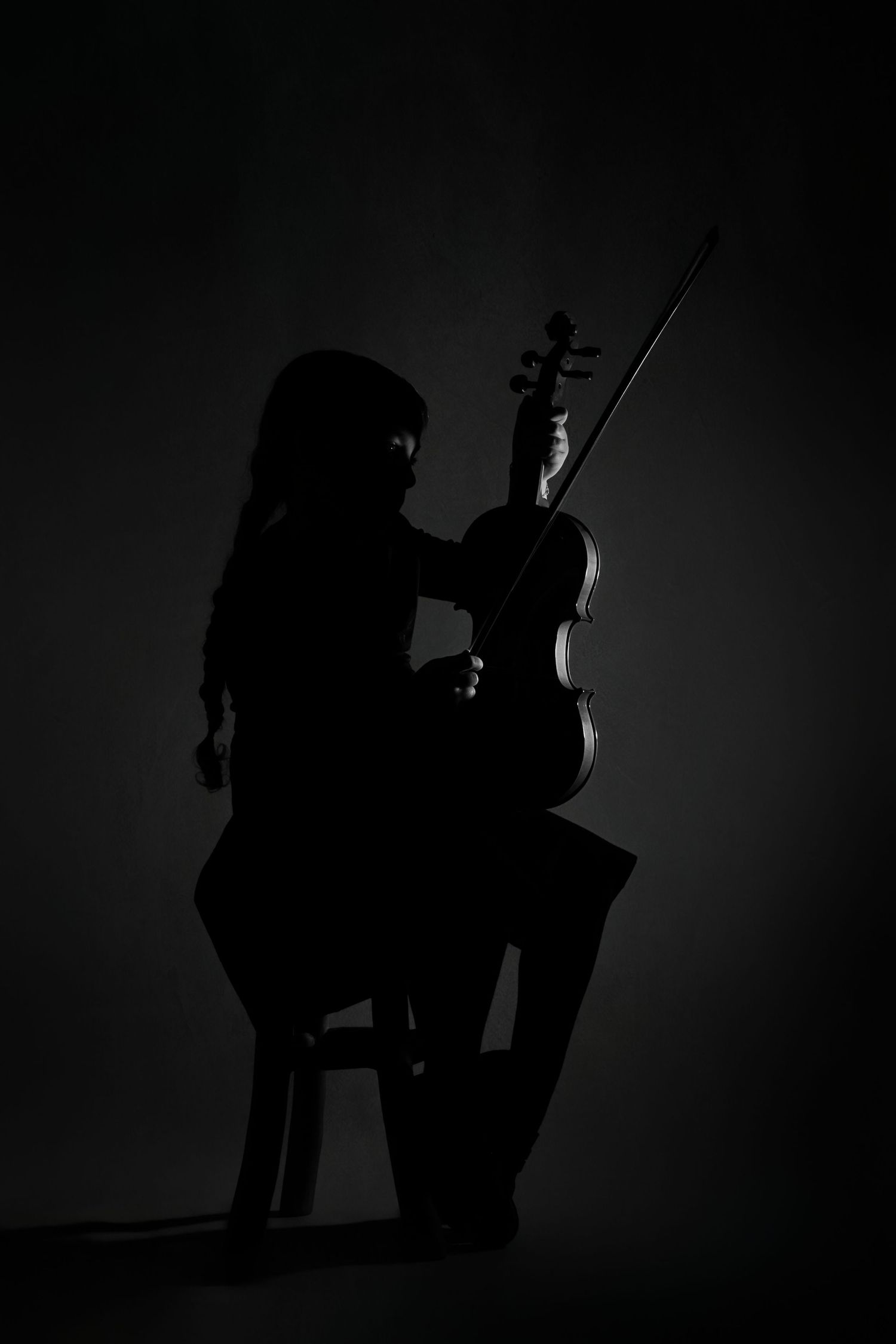 Silhouetted figures play musical instruments in a dark studio with dramatic backlighting creating a moody atmosphere.
