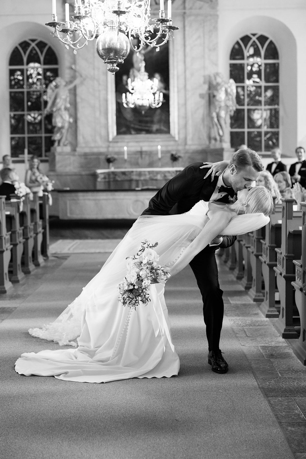 A romantic black and white photo series showing a couple in wedding attire performing a ballroom dance dip in a church.