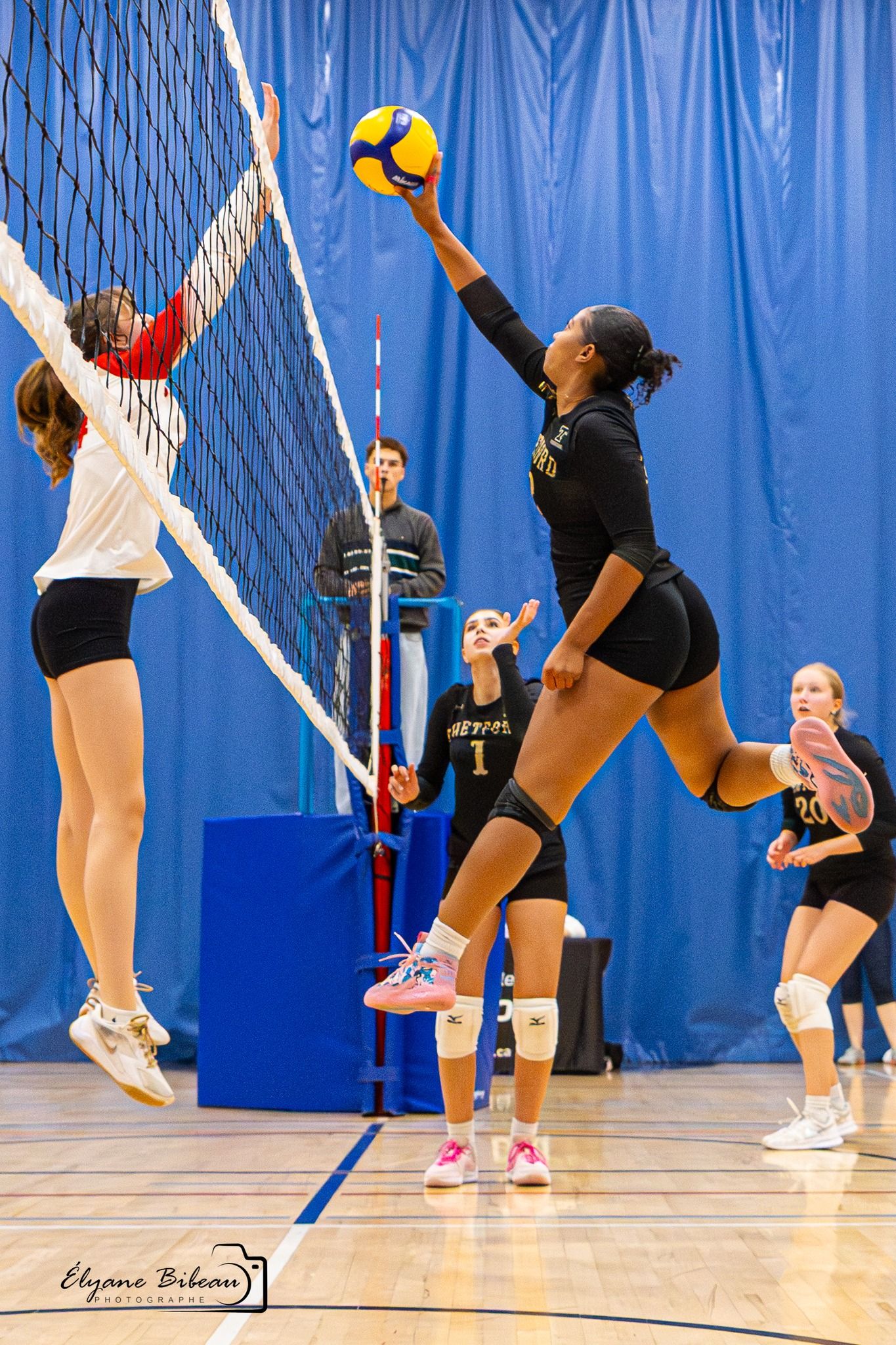 Indoor volleyball players practicing setting and spiking drills in a blue-walled gymnasium with white nets.