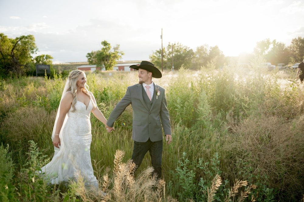 A couple walks through a sunlit meadow at golden hour while holding hands in their wedding attire.