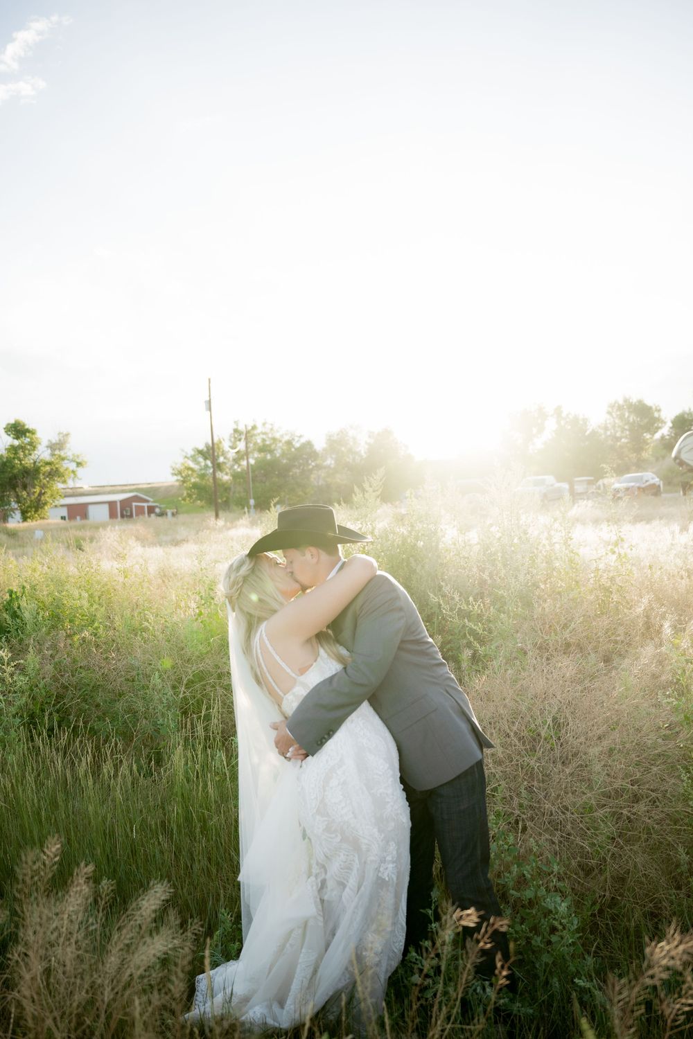 A couple embraces in a sunlit field of tall grass during a romantic outdoor wedding photoshoot at golden hour.