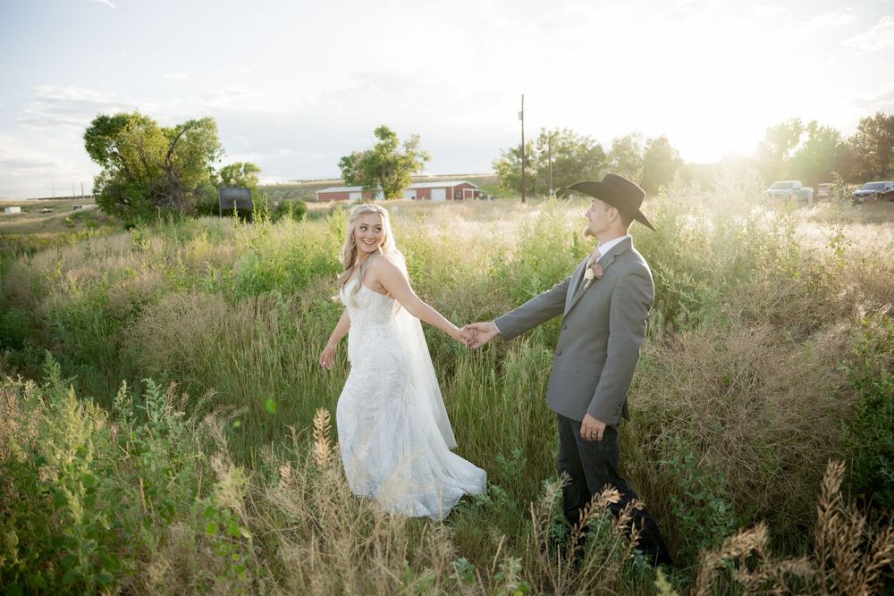 A couple walks through a sunlit meadow during a golden hour wedding photoshoot.