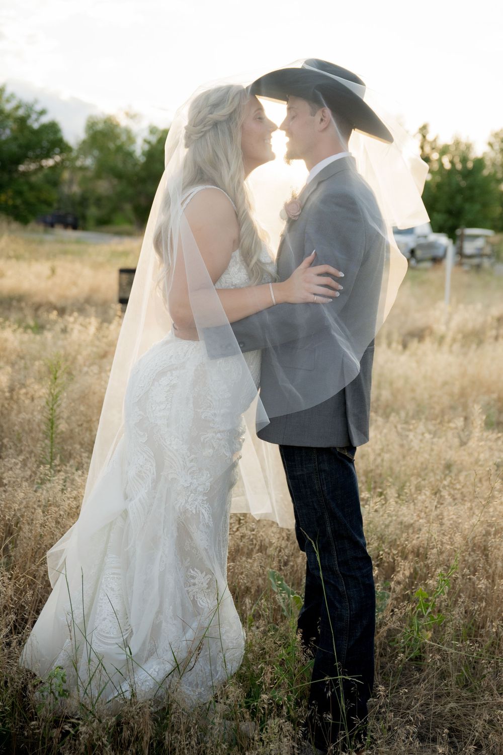 Romantic wedding couple embraces in a sunlit meadow during golden hour as her white dress flows in the breeze.