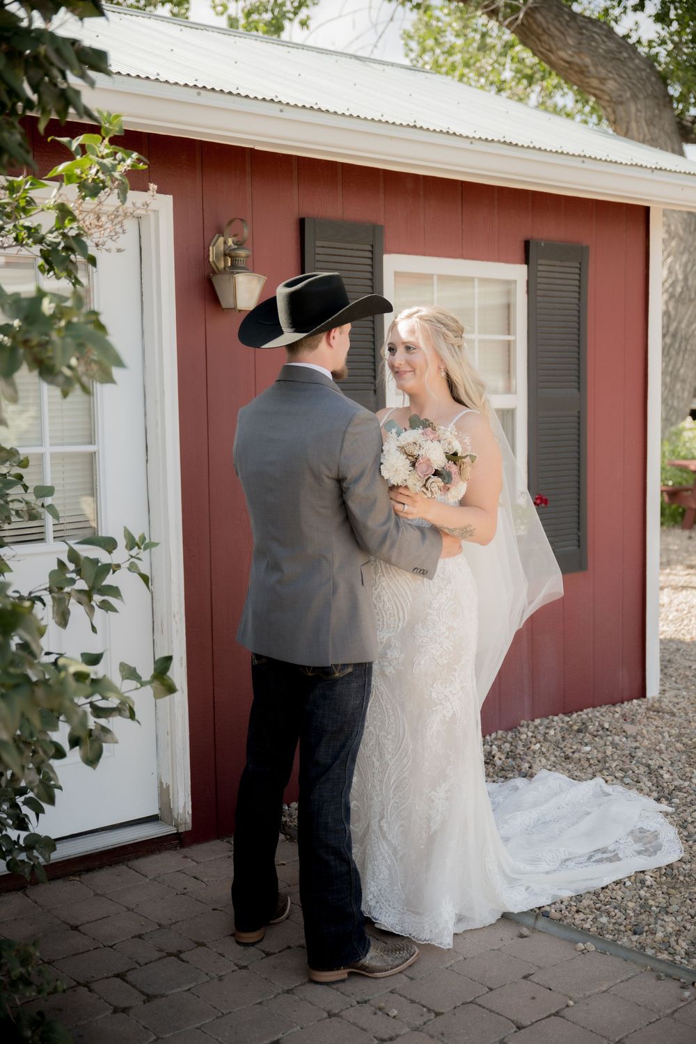 A couple shares an intimate moment outside a rustic red barn building during their country-style wedding ceremony.