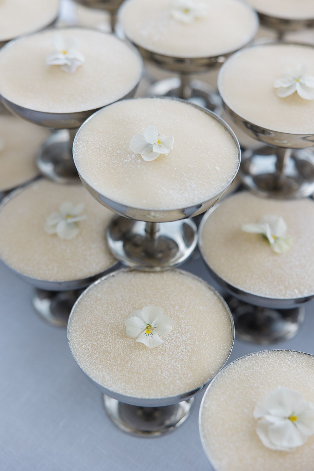 Small white flowers delicately garnish creamy desserts served in elegant silver pedestal dishes.