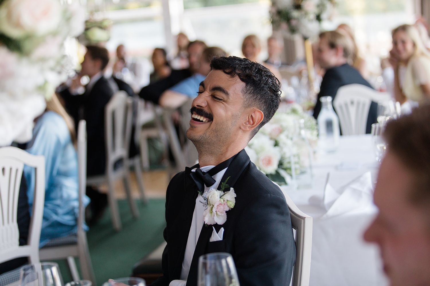 Wedding guests laugh and enjoy themselves during a reception celebration under a white tent.