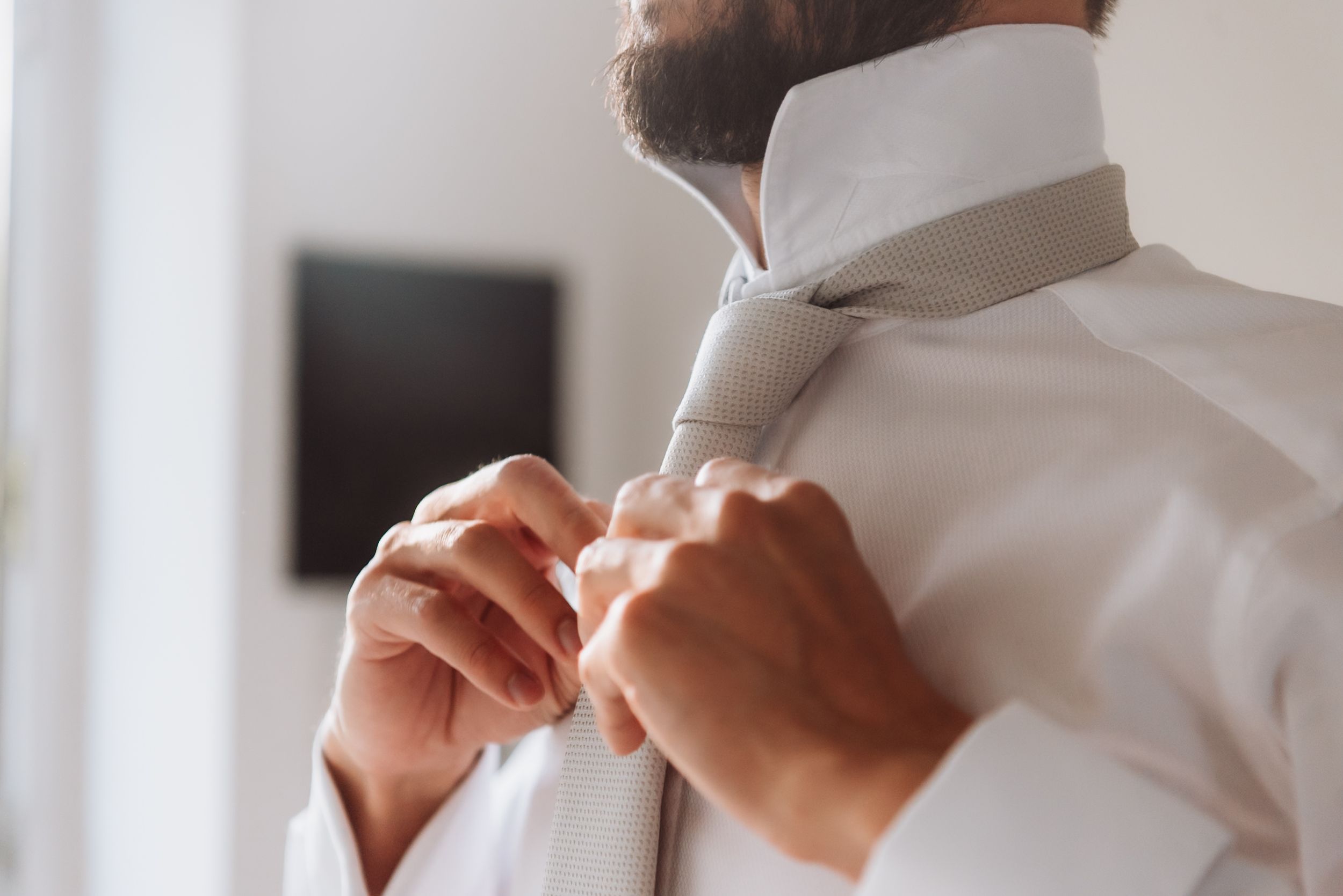 A groom adjusts his boutonniere flower while getting ready for a wedding ceremony.