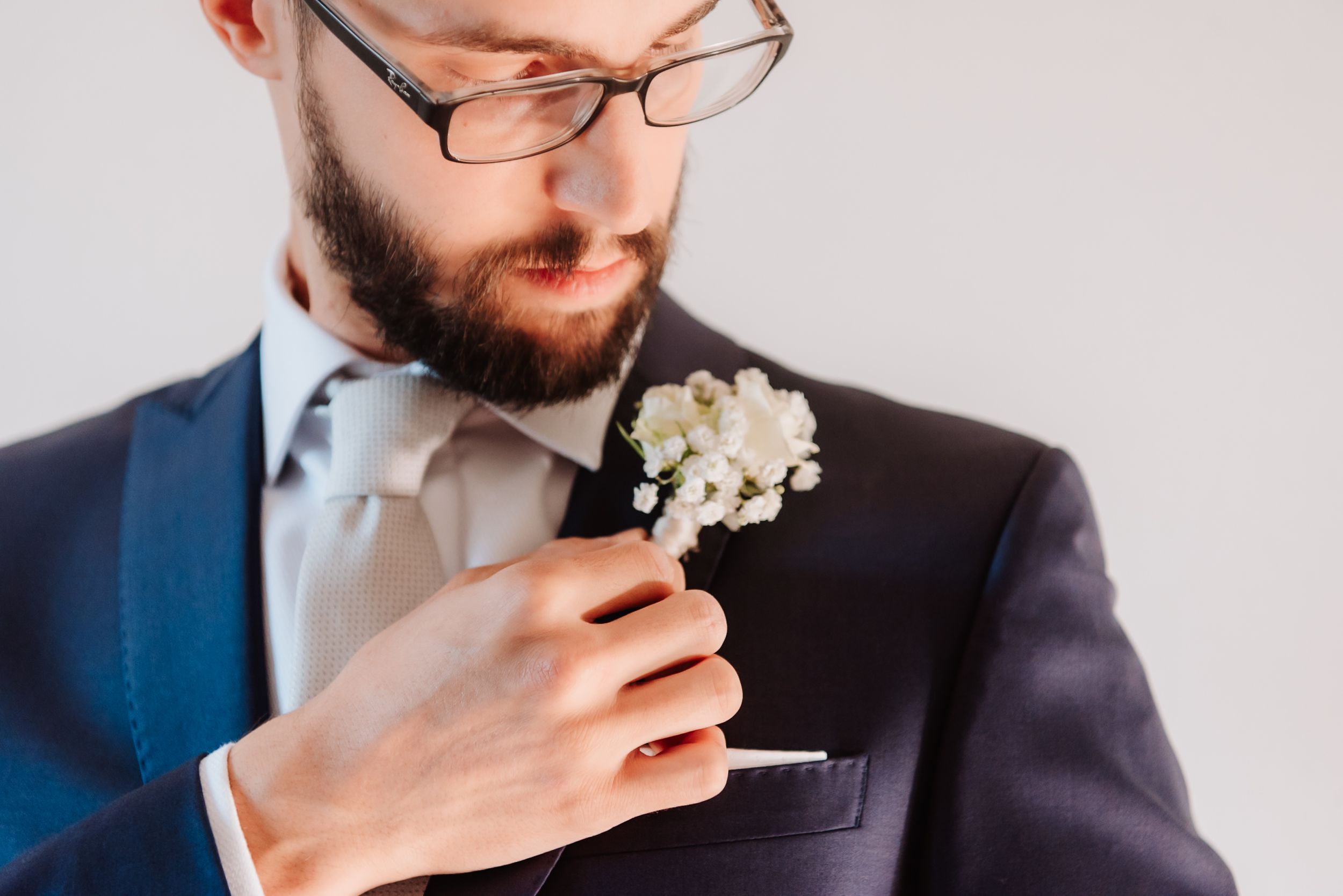 Close-up view of hands pinning a white floral boutonniere onto a suit lapel.