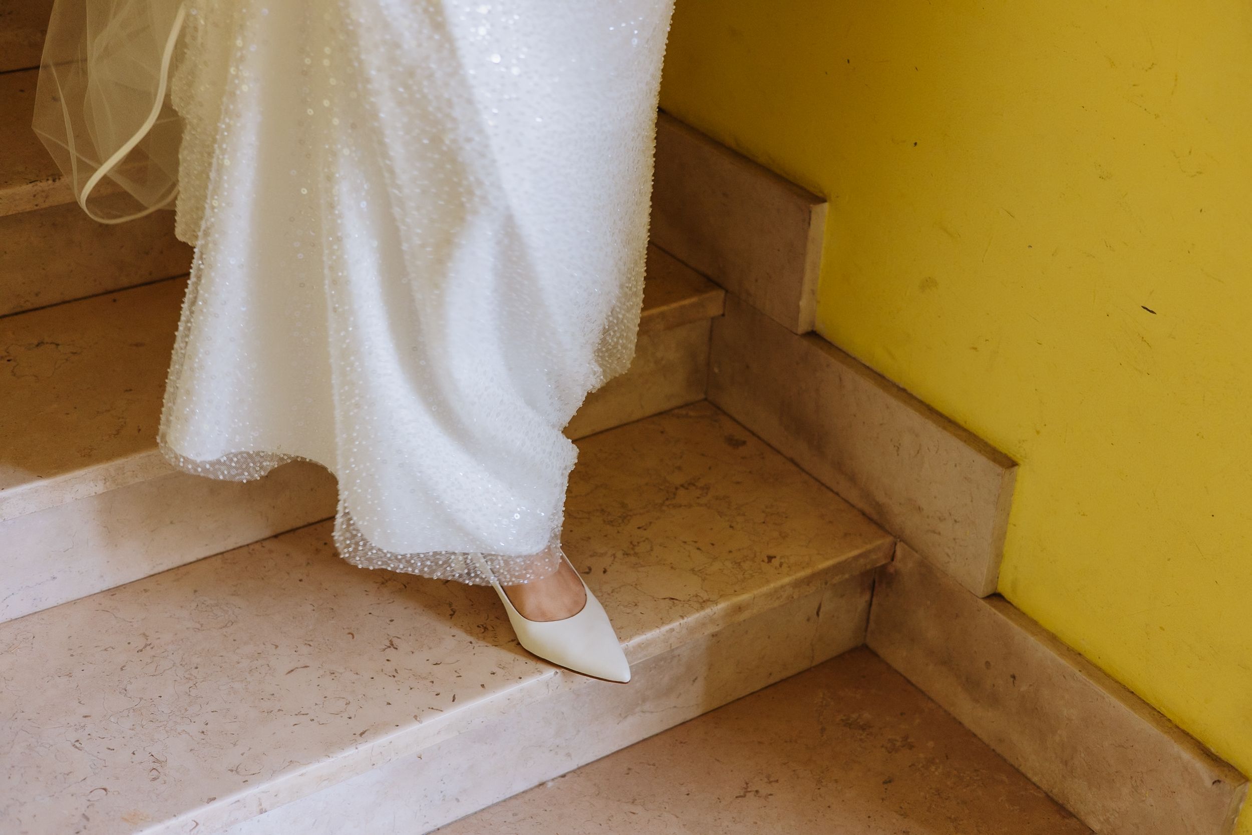 A white curtain hangs against a yellow wall next to a wooden staircase in a bright interior space.