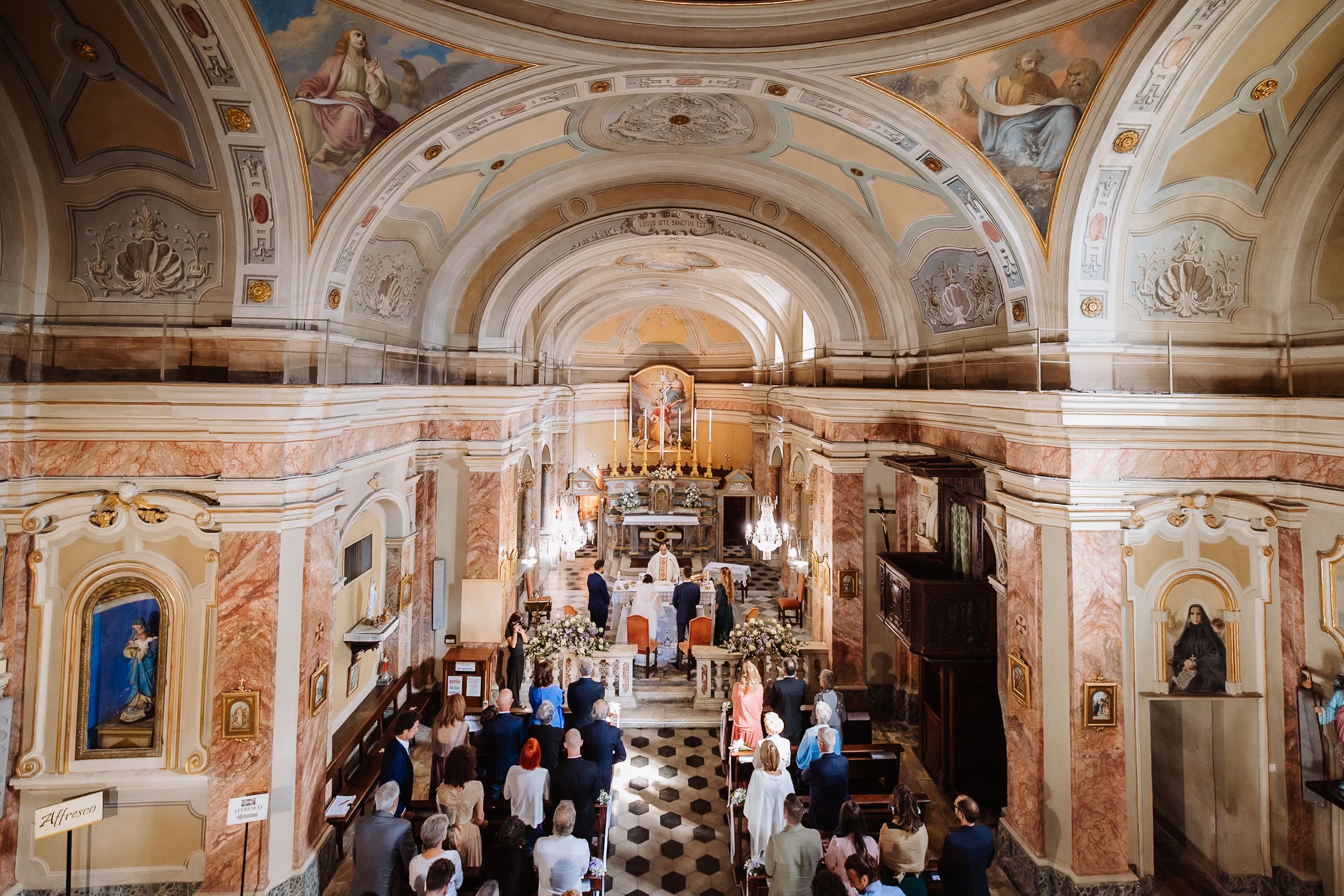 Panoramic view of an ornate baroque church interior with pink walls, frescoes, and golden architectural details.