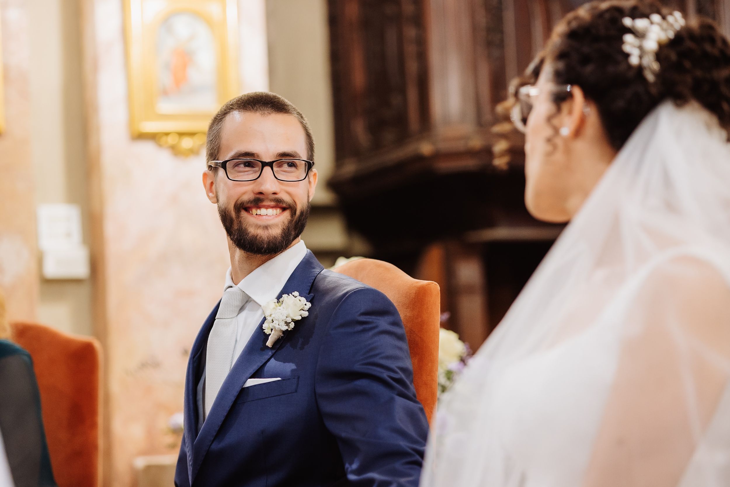 A joyful moment captured during a wedding ceremony in a church with warm lighting and floral boutonniere details.