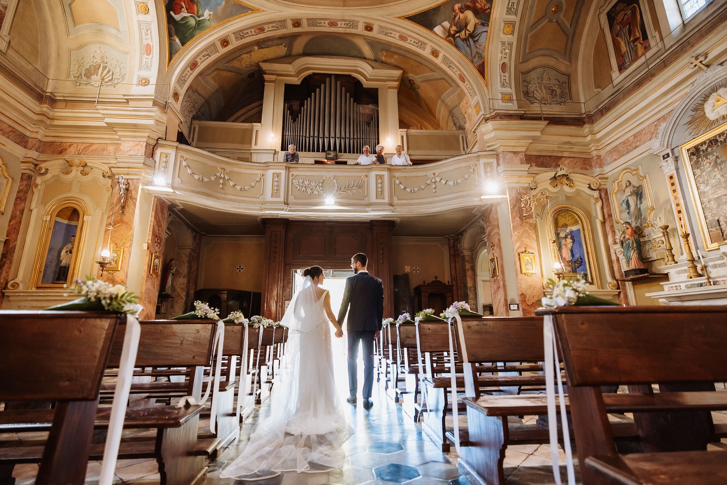 Panoramic view of ornate baroque church interior with white pews and floral decorations for wedding ceremony.