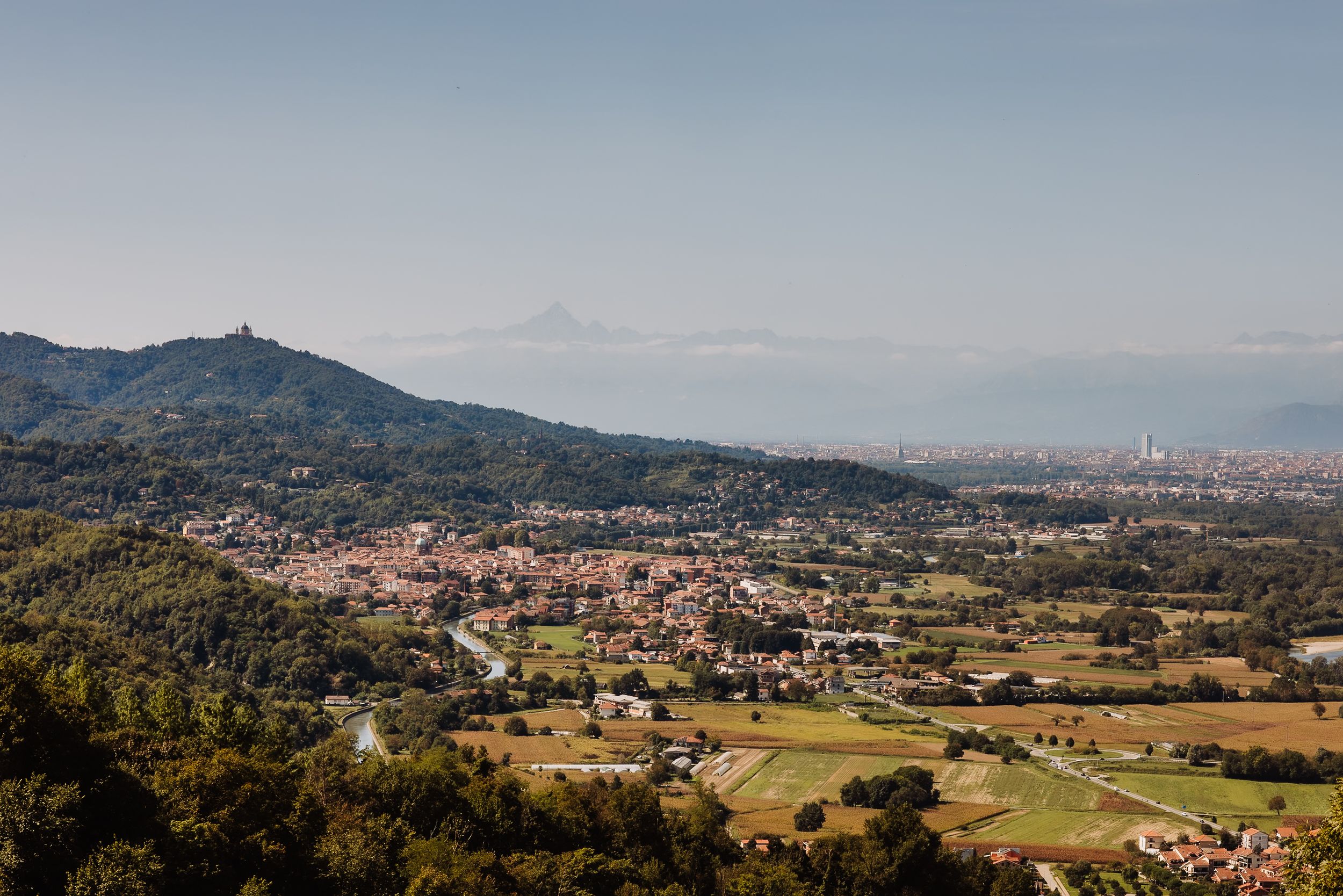 Panoramic aerial view of rolling green hills and mountains with scattered buildings and settlements in a rural landscape.