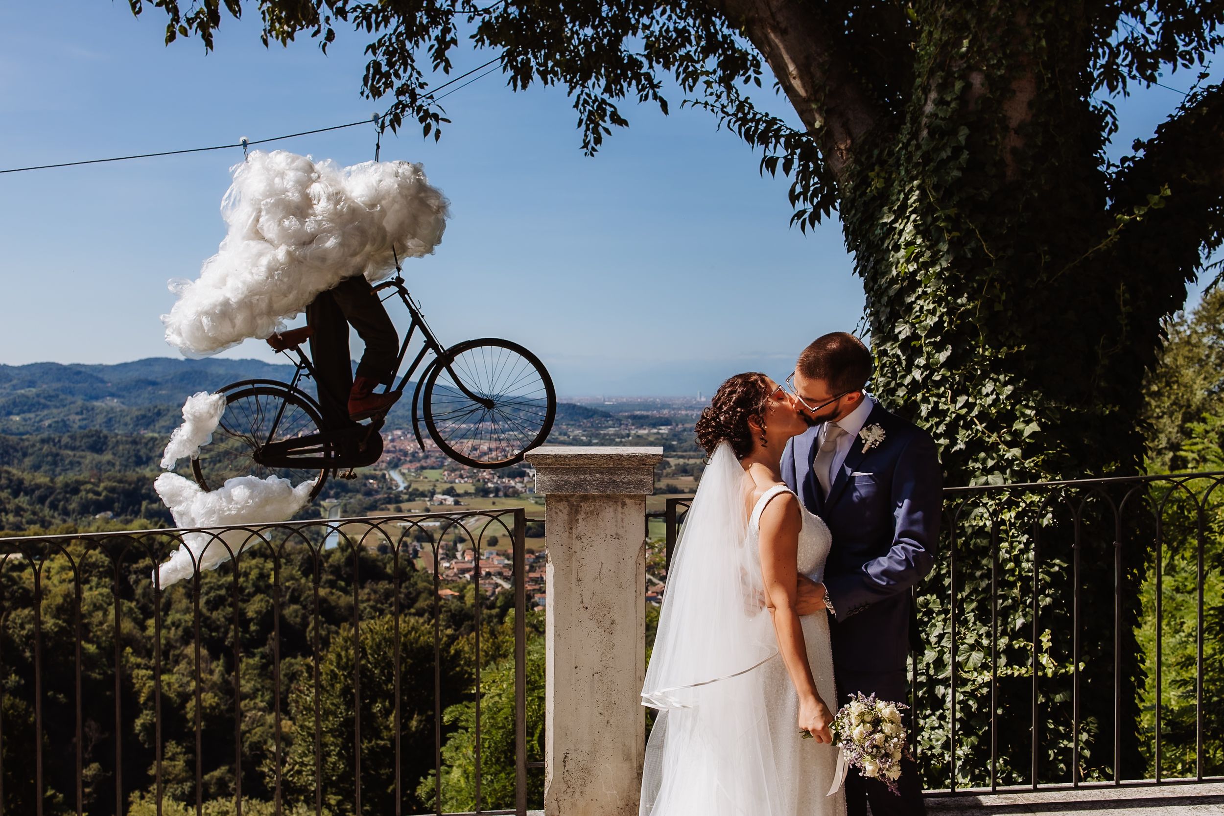 A romantic wedding couple embraces in an outdoor garden setting with scenic mountain views in the background.