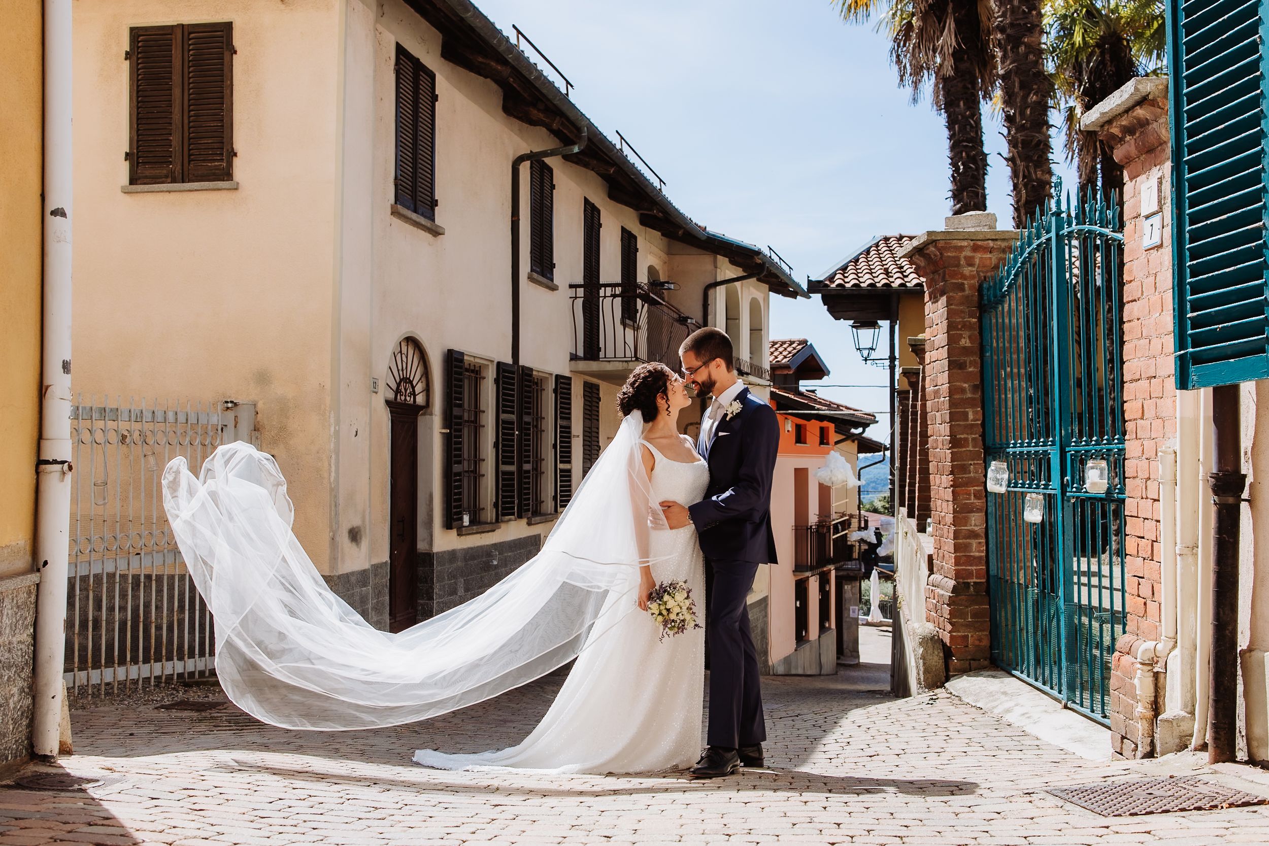 A flowing white wedding dress train sweeps across a charming cobblestone street in an Italian village setting.
