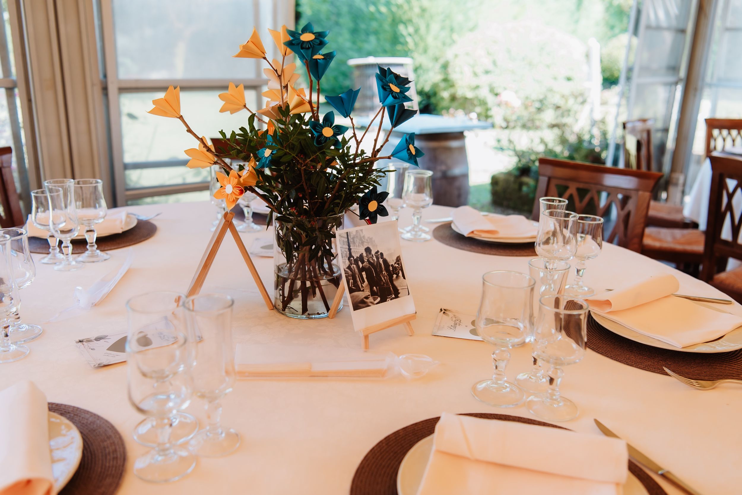 Elegant table settings with white linens, wine glasses, and small floral centerpieces in a bright dining room.