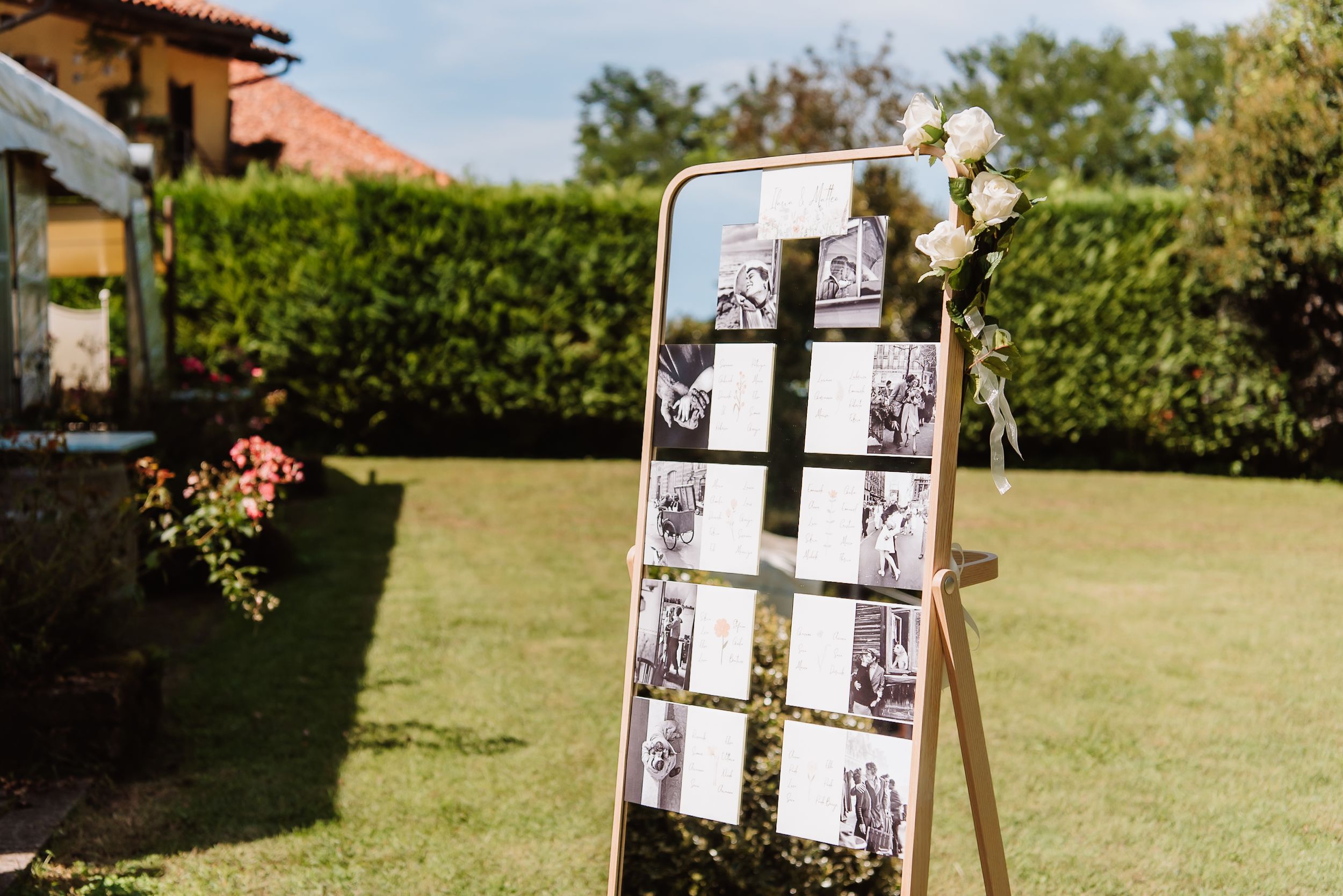Wedding ceremony decor features a rustic wooden display stand with vintage photos in a sunny garden setting.