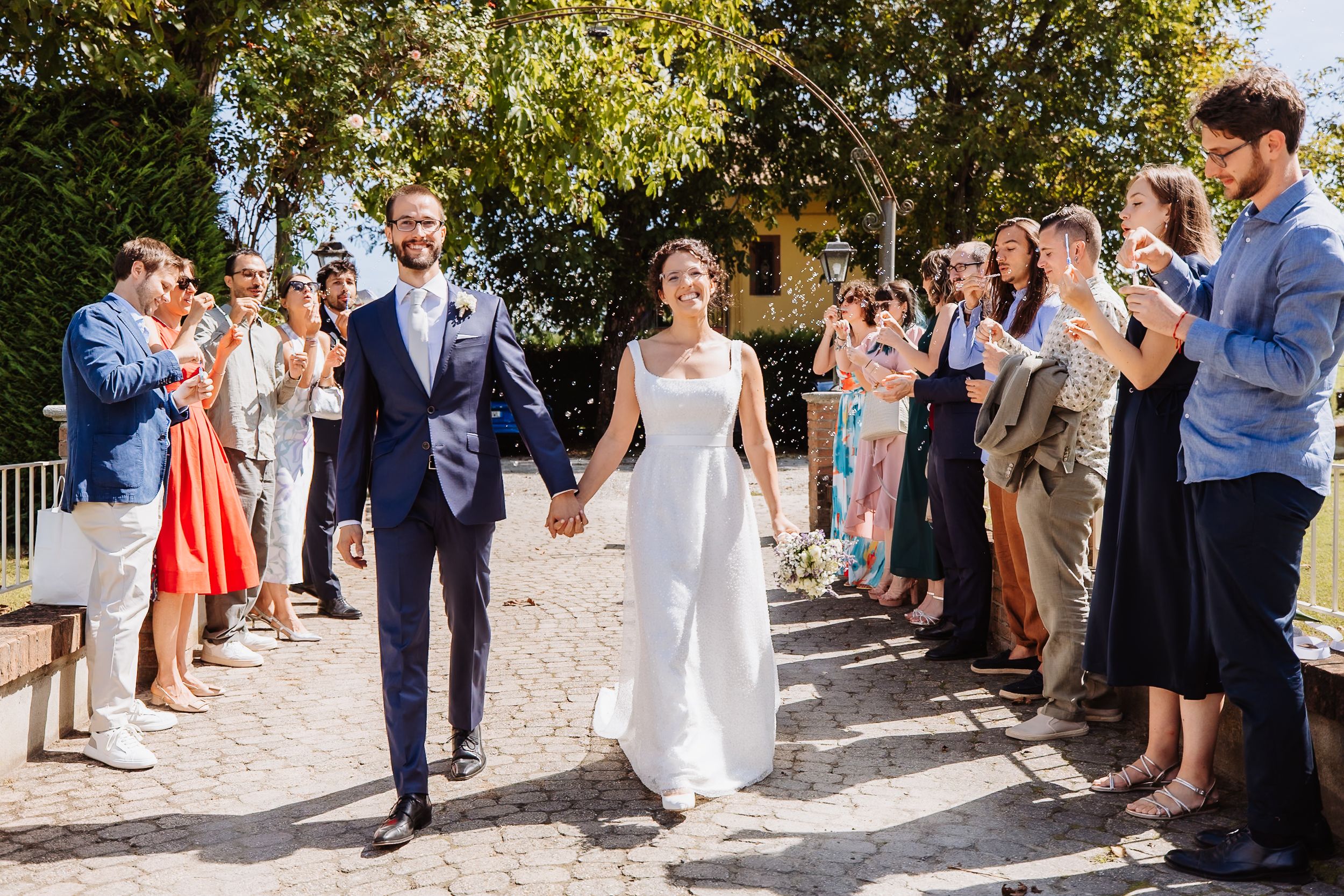Wedding guests line up outdoors to celebrate during a sunny summer celebration.