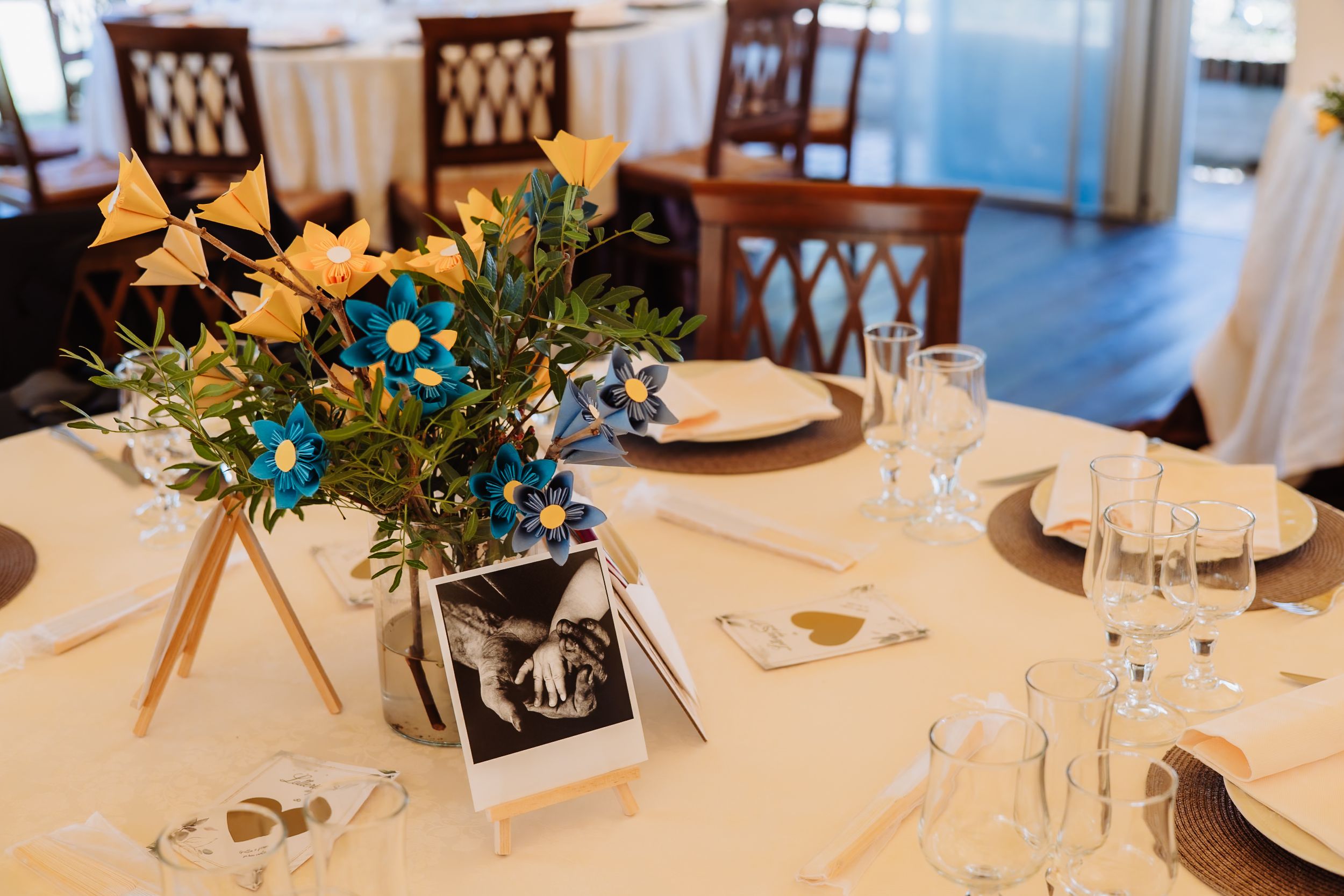 Elegant wedding reception tables with white linens, floral centerpieces, and dark wooden chairs in a bright dining room.