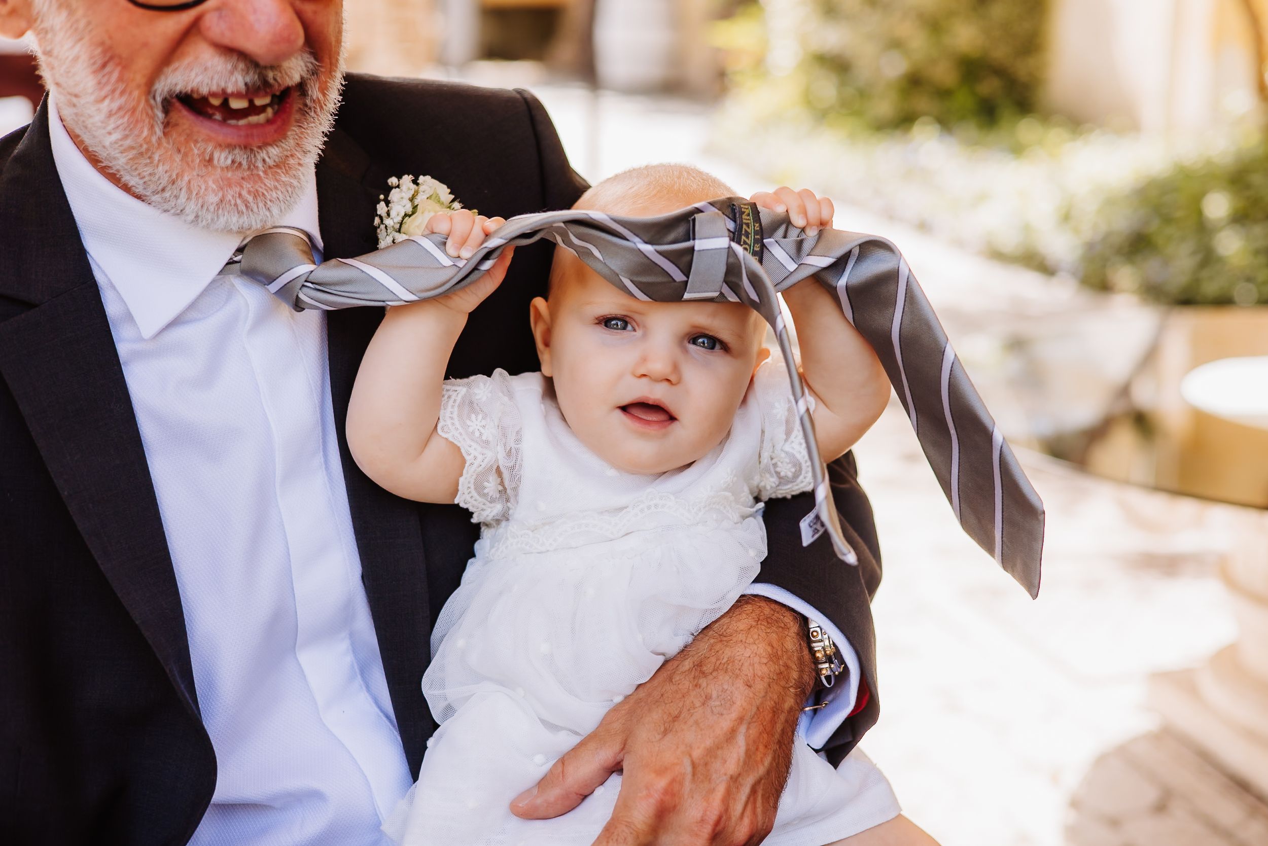 A small baby in white dress being held while wearing a decorative headpiece at a formal event.